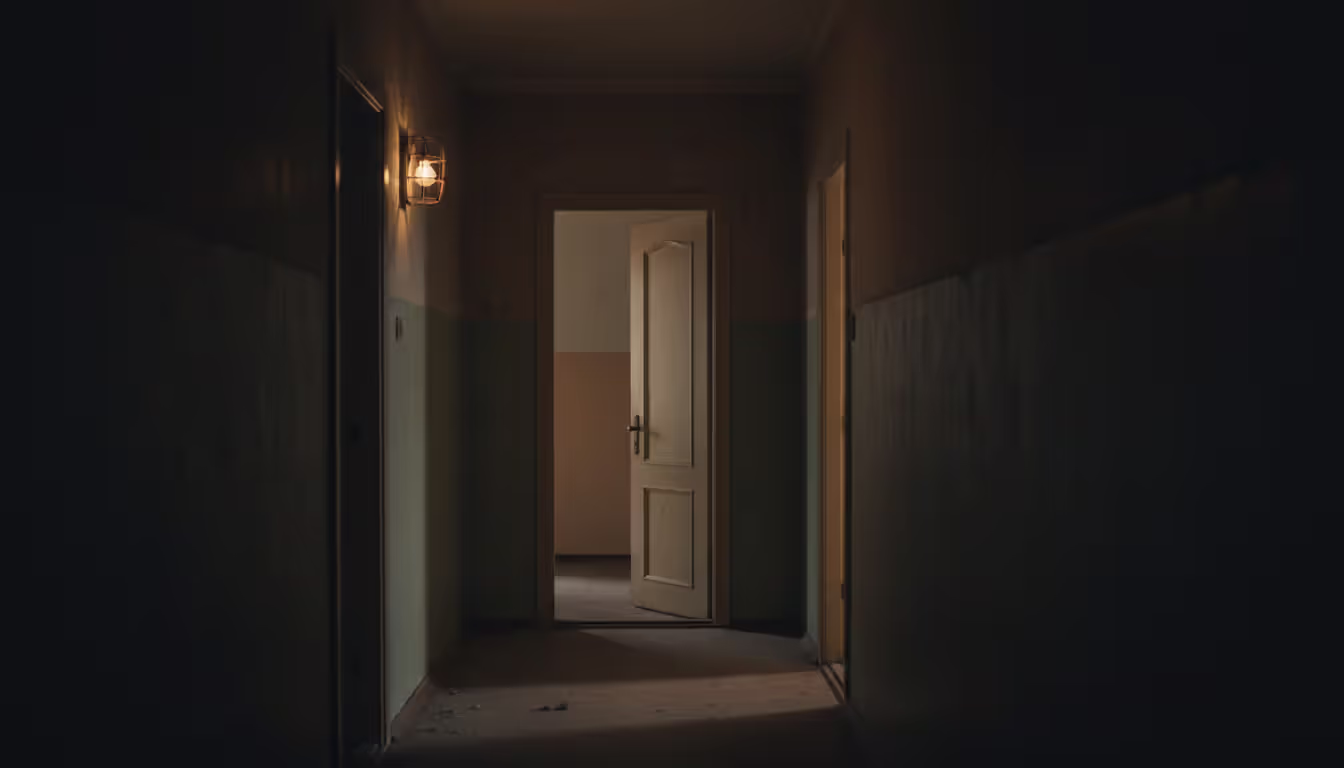 Dimly lit apartment hallway with a slightly open front door creating an unsettling atmosphere