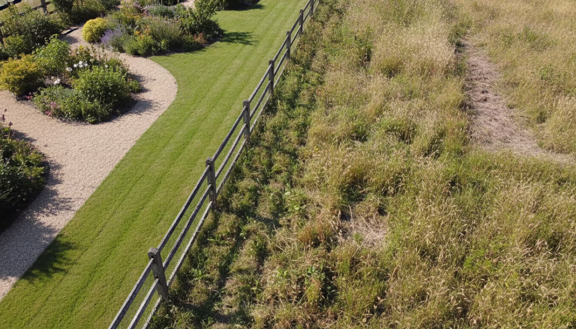Wooden fence dividing two neighboring land plots, one maintained with mowed lawn and the other overgrown with tall grass, suburban setting, daylight