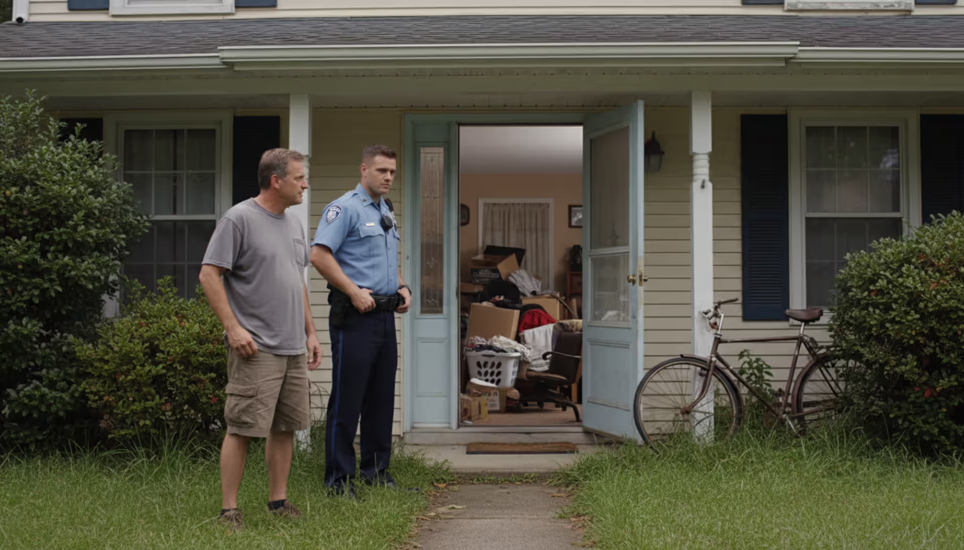 Police officer and homeowner standing outside cluttered house with open door during property inspection